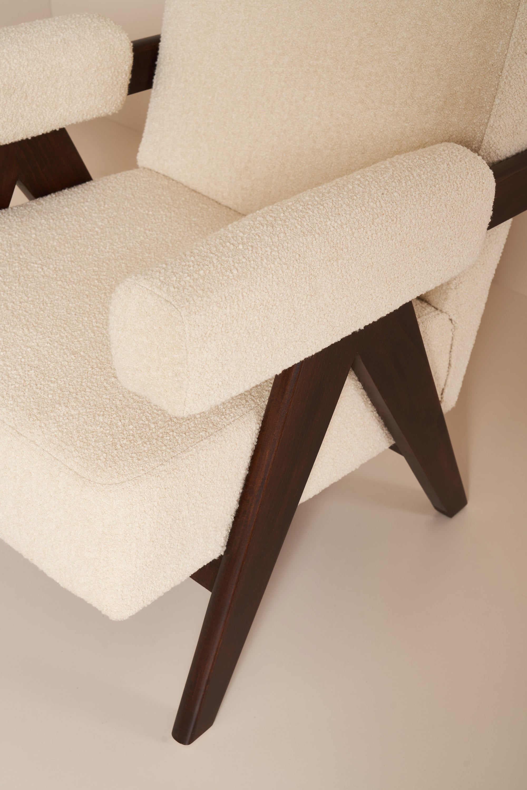 Close-up of a chair with beige fabric and dark wooden legs on a neutral background