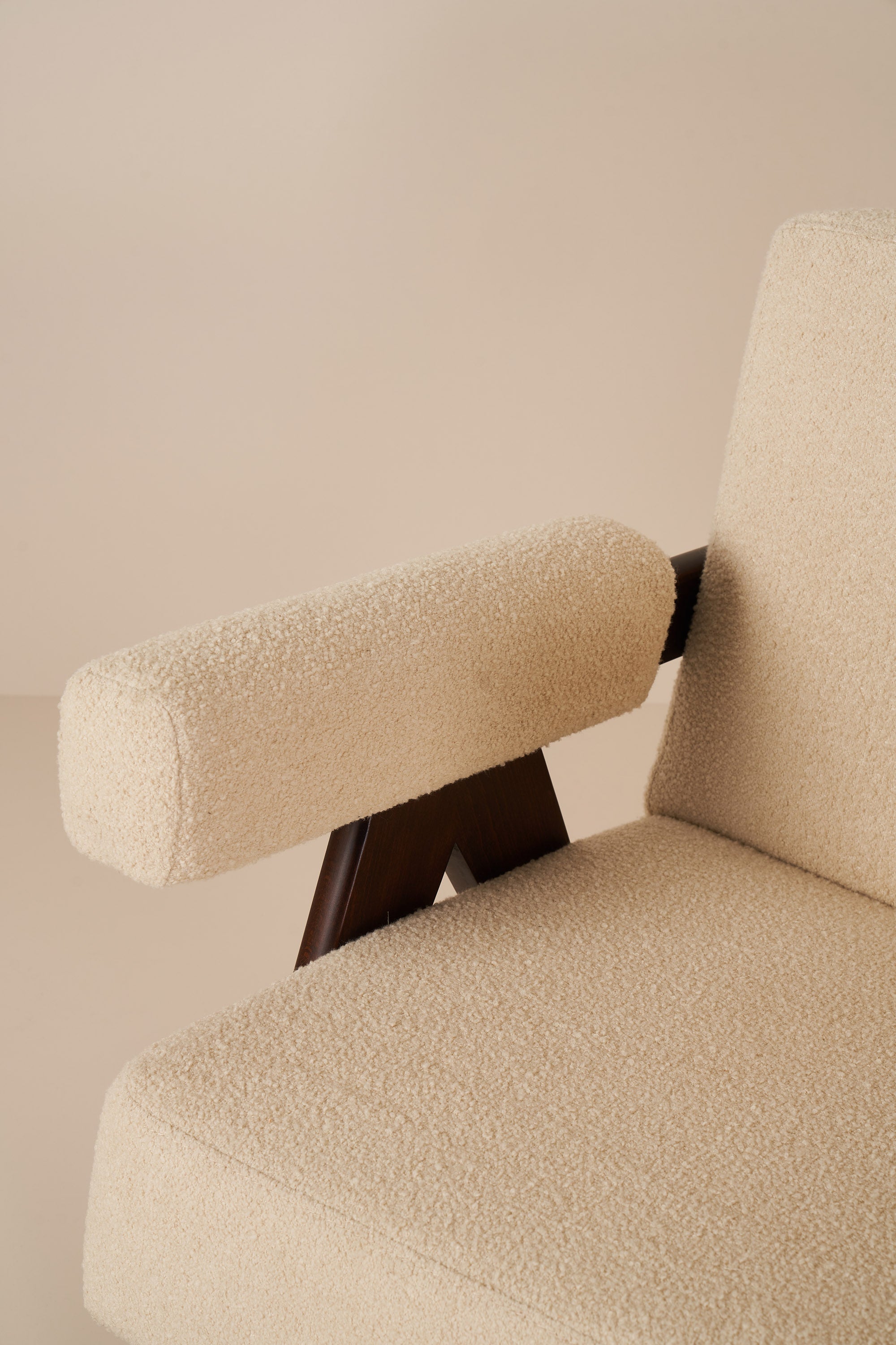 Beige armchair with wooden armrests against a beige wall