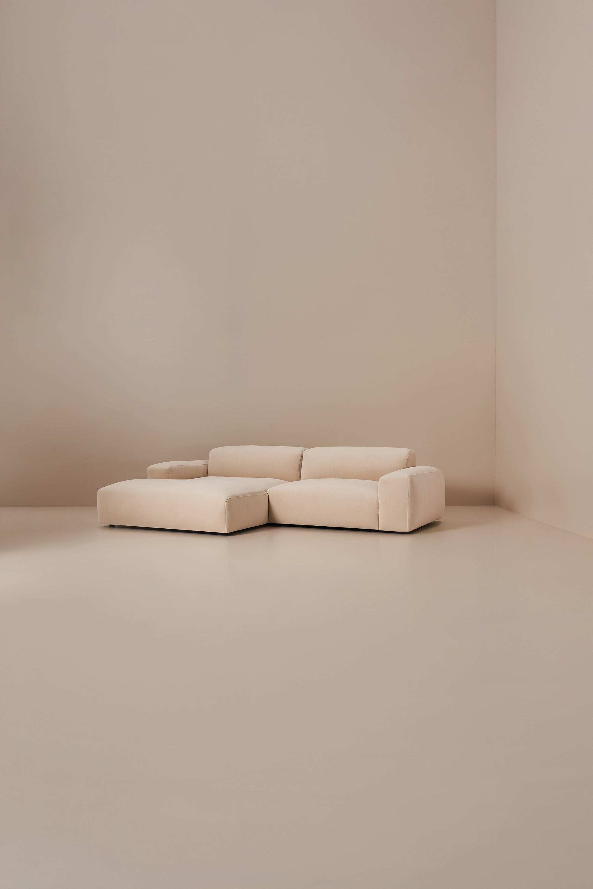 Beige sectional sofa in a minimalistic room with beige walls and floor.