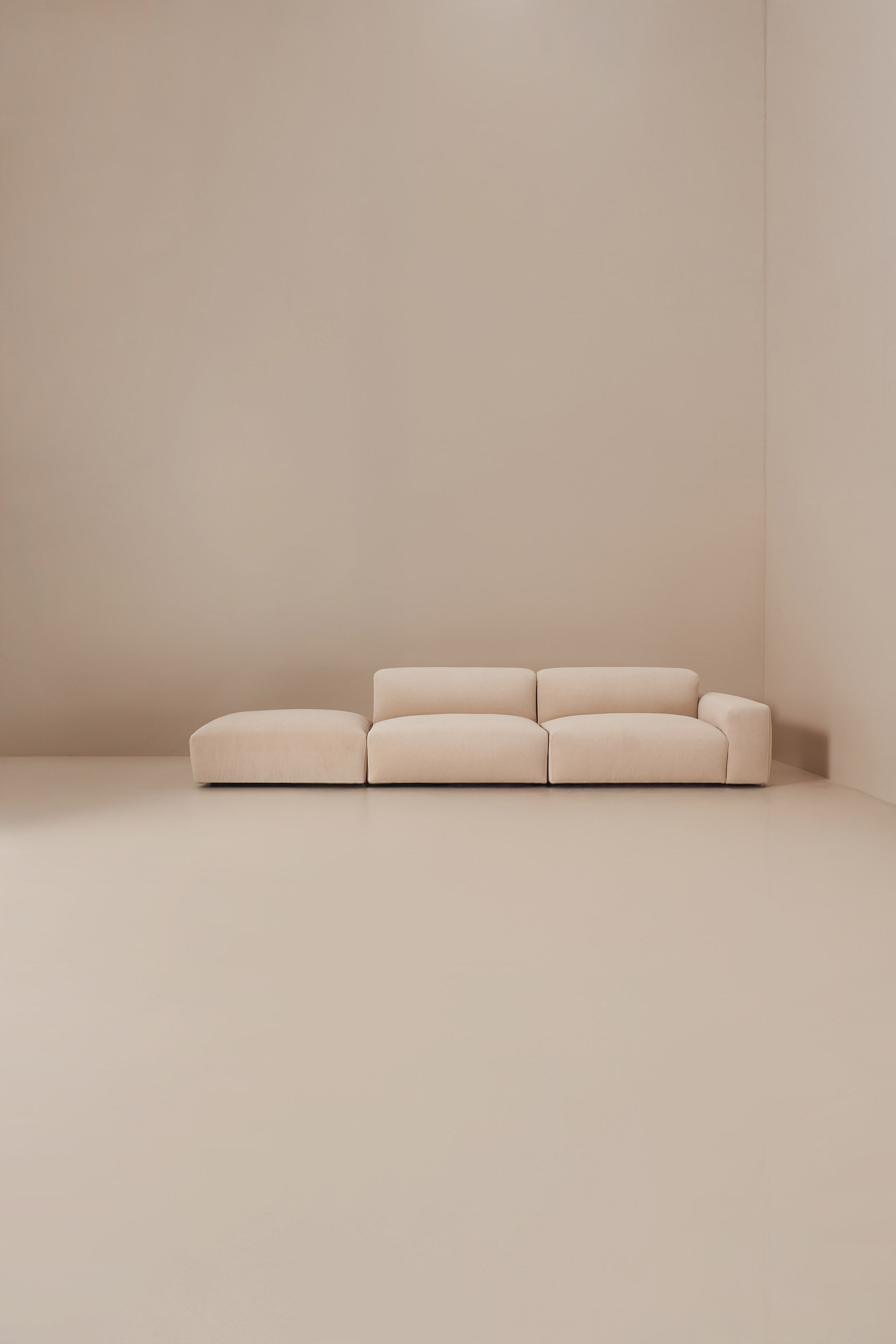 Beige modular sofa in a minimalistic room with beige walls and floor.