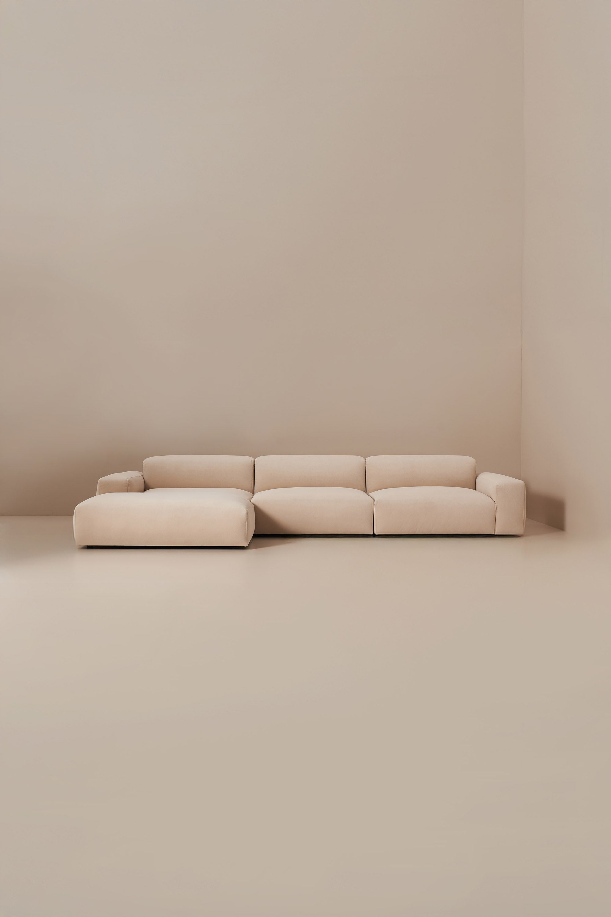 Beige sectional sofa in a minimalistic room with beige walls and floor.