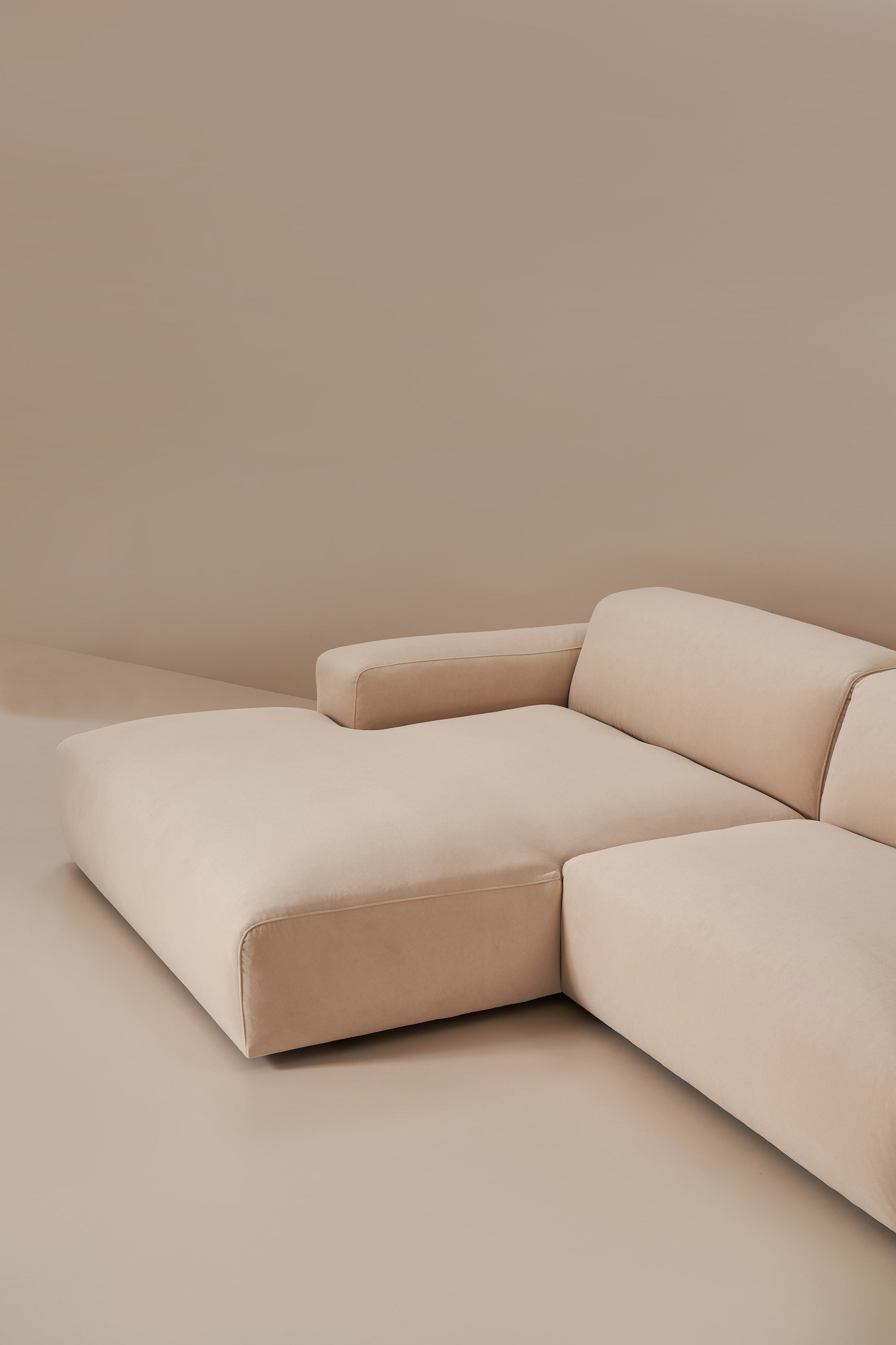Beige sectional sofa in a minimalistic room with a plain wall.