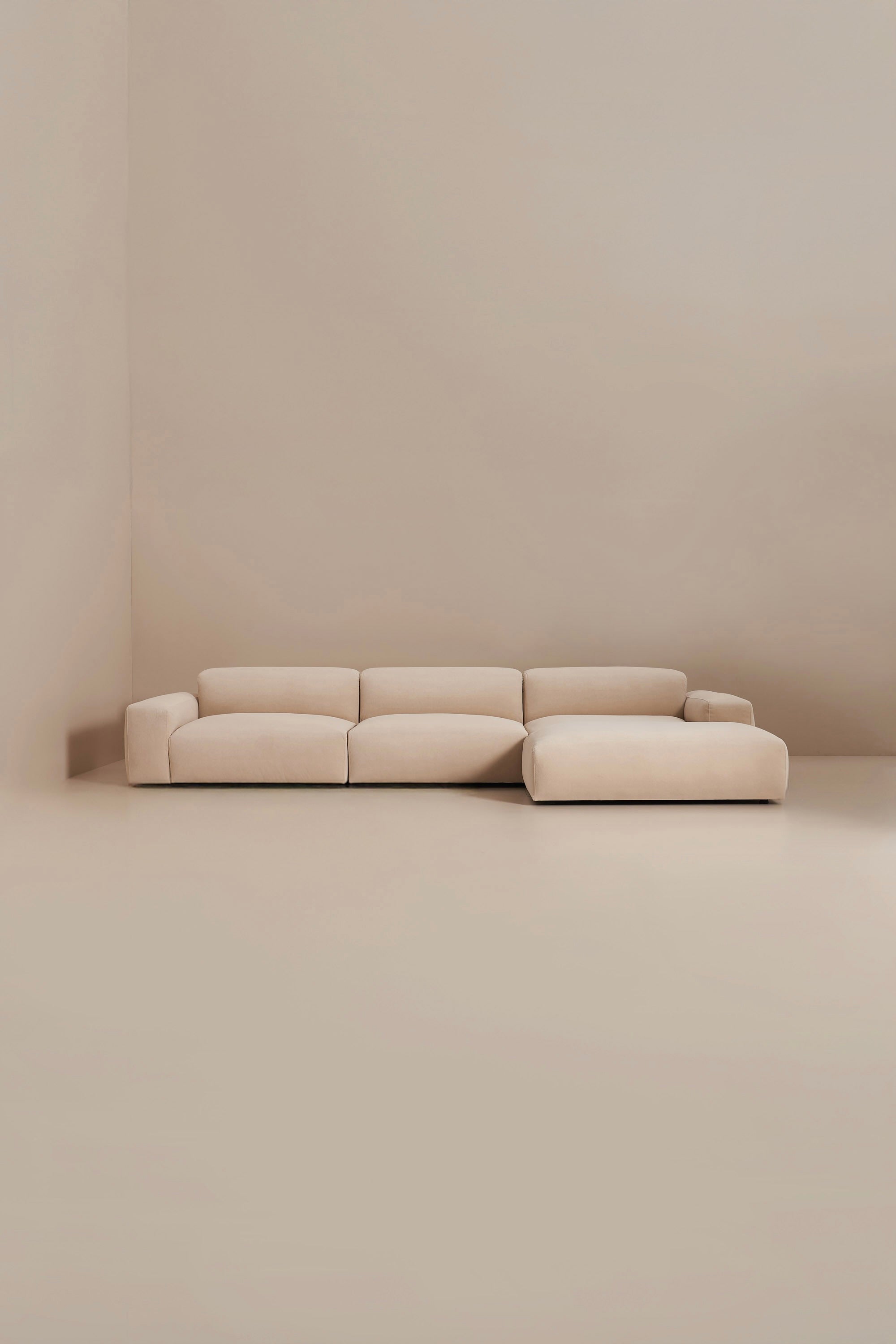 Beige sectional sofa in a minimalistic room with beige walls and floor.